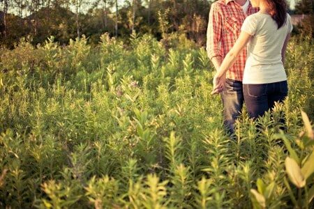 Couple se tenant par la main debout dans un champs