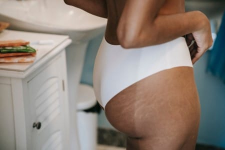 Femme en culotte près d'une serviette hygiénique dans sa salle de bain