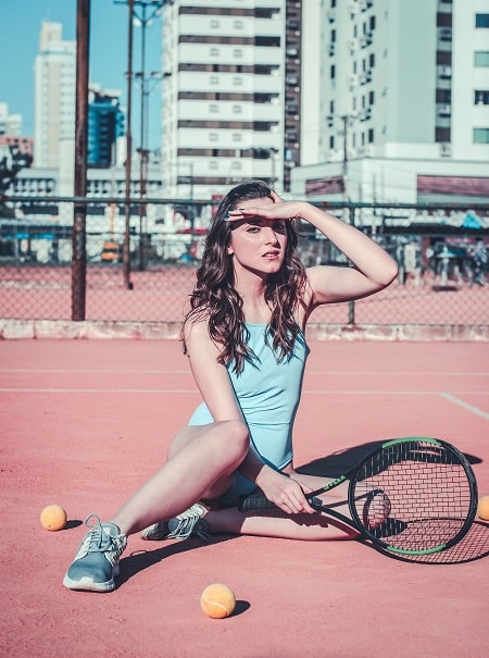 Femme assise sur le sol et tenant une raquette de tennis